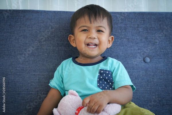 Fototapeta Cute little boy sitting on the sofa with teddy bear