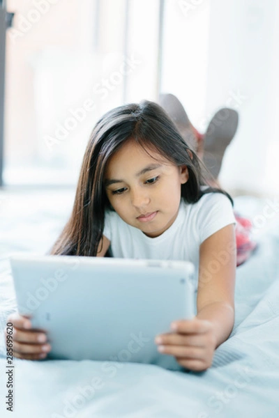 Obraz Young girl lying on bed using her tablet