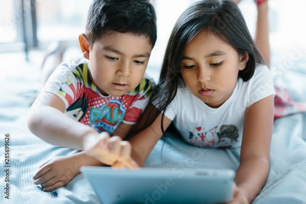 Obraz Two siblings lying on bed using a tablet