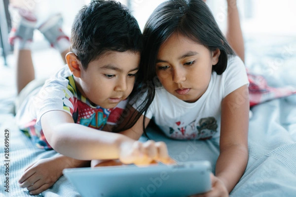 Obraz Two siblings lying on bed using a tablet