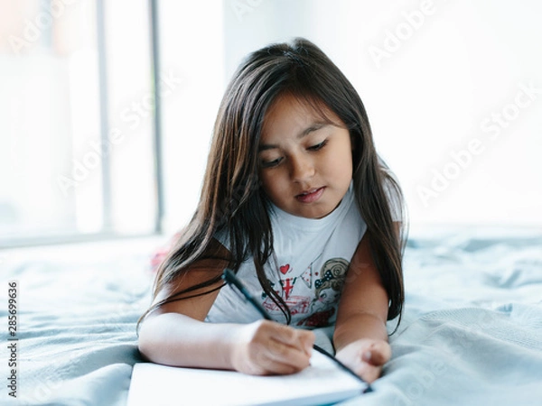 Obraz Young girl lying on bed writing on a notebook