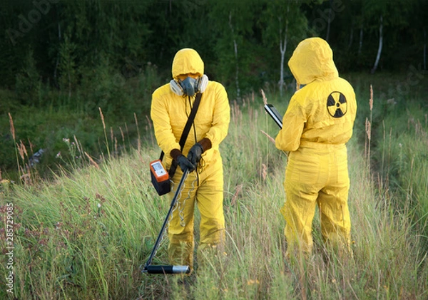 Fototapeta Two dosimetrist  in protective suite and mask with geiger counter measuring radiation level in danger zone