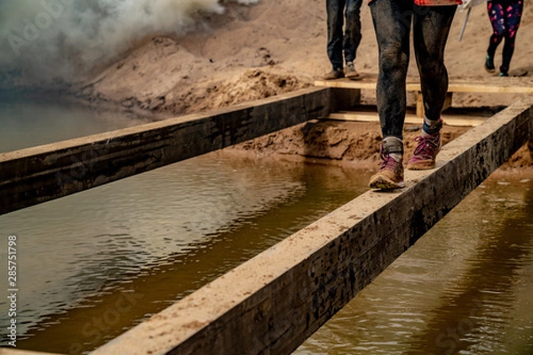 Fototapeta Girl crosses an obstacle at a sporting event. Only legs. Walking along a narrow beam above the water