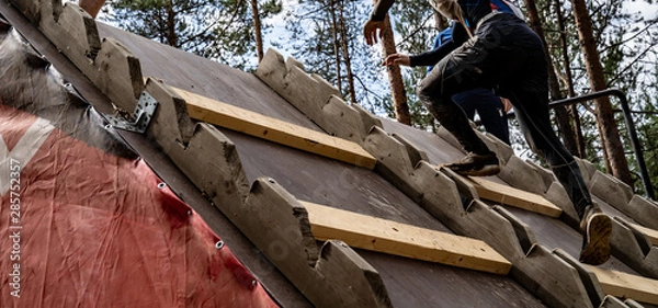Fototapeta A man climbs an obstacle at a sporting event. He hard goes up on top of obstacle. Sport activity in the forest