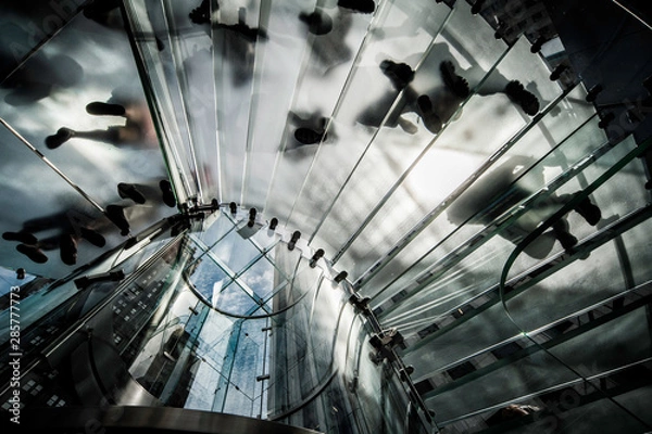 Fototapeta People walking up and down a glass staircase seen from below appear as silhouettes against the light. No faces