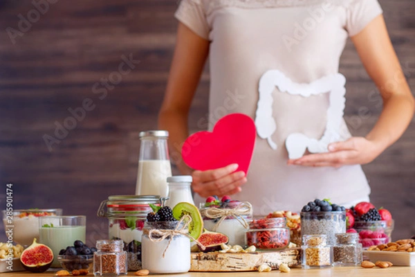 Fototapeta Female is holding figures of heart and intestines. Summer breakfast with organic yogurts fruits, berries and nuts. Nutrition that promotes good digestion and functioning of gastrointestinal tract.