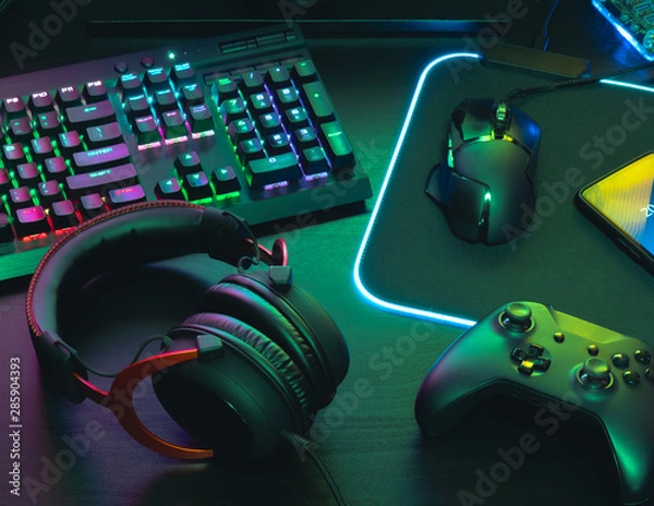 Fototapeta gamer work space concept, top view a gaming gear, mouse, keyboard, joystick, headset, mobile joystick, in ear headphone and mouse pad on black table background.
