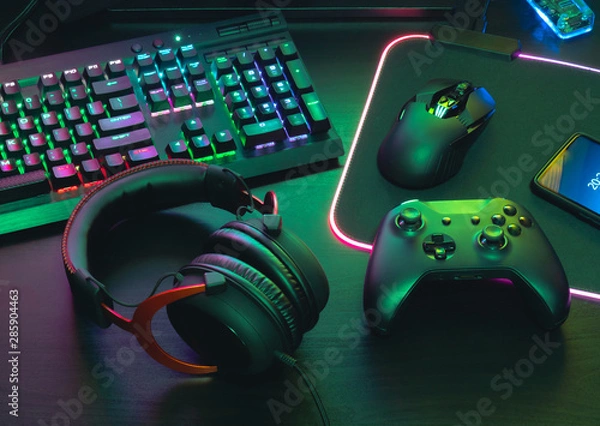 Fototapeta koncepcja przestrzeni roboczej dla graczy, widok z góry sprzęt do gier, mysz, klawiatura, joystick, zestaw słuchawkowy, mobilny joystick, słuchawki douszne i podkładka pod mysz na czarnym tle stołu.