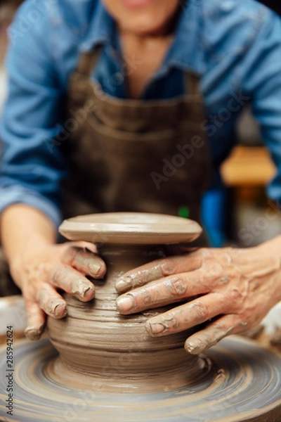 Fototapeta Senior female potter working on pottery wheel while sitting  in her workshop