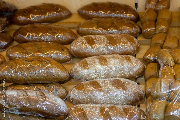 Fototapeta Loafs of fresh rye bread in flour sprinkles wrapped in plastic film on a bakery counter
