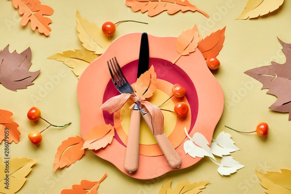 Fototapeta Table setup for Autumn celebration. Bright plastic plate on yellow paper with paper Autumn leaves
