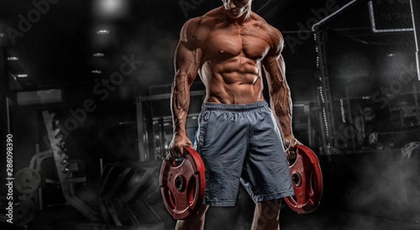 Fototapeta Young male athlete bodybuilder posing and doing sports exercises in the gym