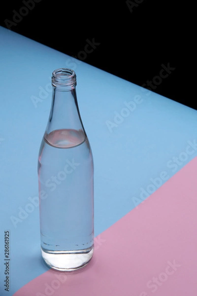 Fototapeta Glass bottle water on a bright pink and blue background close up