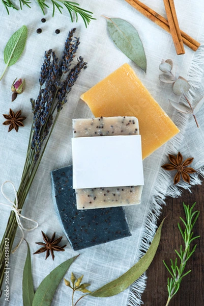 Obraz three bars of soap on a white cloth with natural ingredients, handmade soap with blank label, mockup label flat lay, rosemary, eucalyptus, star anise, lavender, peppercorns, cinnamon, rosebud, sage