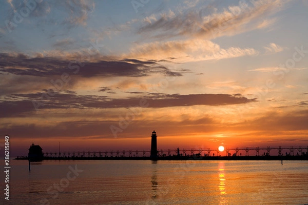 Fototapeta The sun makes a perfect ball of light as it sets over Lake Michigan behind the Grand Haven Pierhead Light, Grand Haven, MI