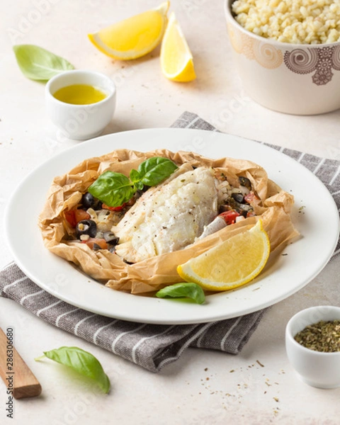 Obraz Fillet of white fish (Pollock, cod, sea bass, Dorada) with olives, tomatoes and lemon, baked in parchment. Traditional French food fish papillot and bulgur