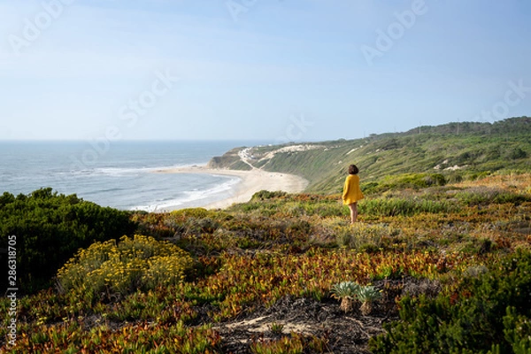 Fototapeta Girl view from the back and side standing on the grass with a view to the beach from the top of a mountain.