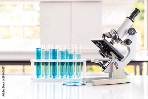 Obraz Closed up microscope with tube and glass in laboratory. Blue chemist in glass tubes on lab white table.