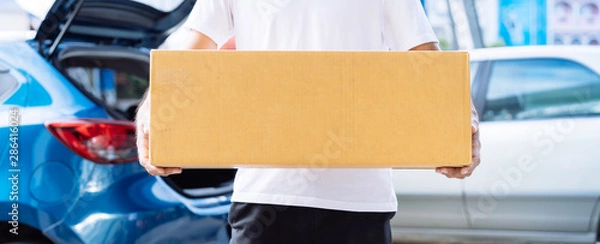 Fototapeta Delivery man carrying cardboard box for sending deliver to customer by transportation system hatchback car, Business of male transport sell part or product service parcel for convenience of customer