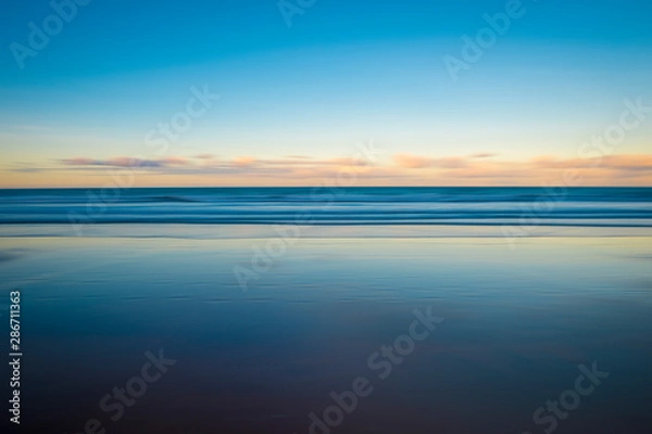 Fototapeta Scenic view of the glassy smooth shore of a deserted beach during the magic hour of sunset