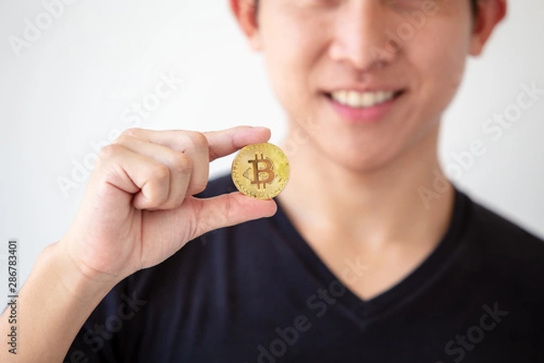 Obraz Young asian man hold golden bitcoin coins in hand. Virtual currency. Crypto currency. New virtual money.
