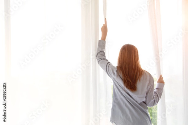 Fototapeta Close up of happy young woman opening window curtains at home. Concept of people ready to start day with fresh life and ready for work. Free copy space.