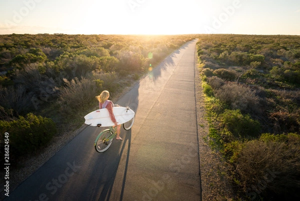 Obraz Beautiful blonde surfer girl on her way to the beach on her bicycle with her surfboard.