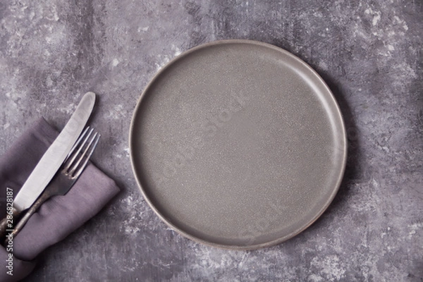 Fototapeta Empty gray plate and cutlery over gray concrete table. Minimalism. Copy space. Top view.