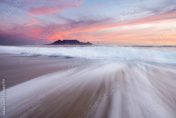 Obraz Table Mountain at sunset as seen from Blouberg with waves crashing on the beach under pink skies.