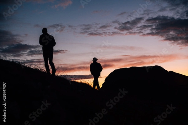 Obraz  Two silhouettes walk on slope towards sunset