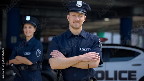 Fototapeta Mili policjanci uśmiechnięci stojąc w pobliżu komisariatu, gotowi do pomocy, rozkazu