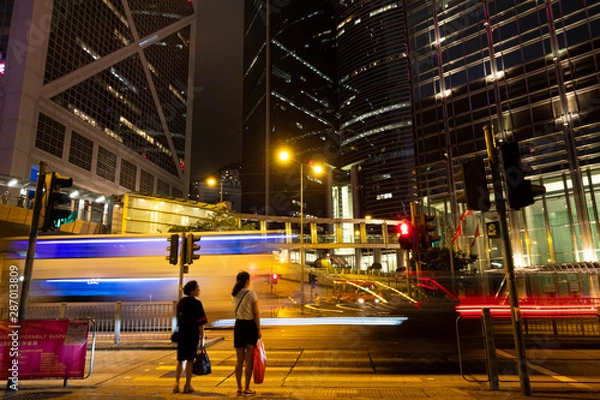 Obraz 近未来都市的な高層ビル群を通過する光る乗り物と通行人たち