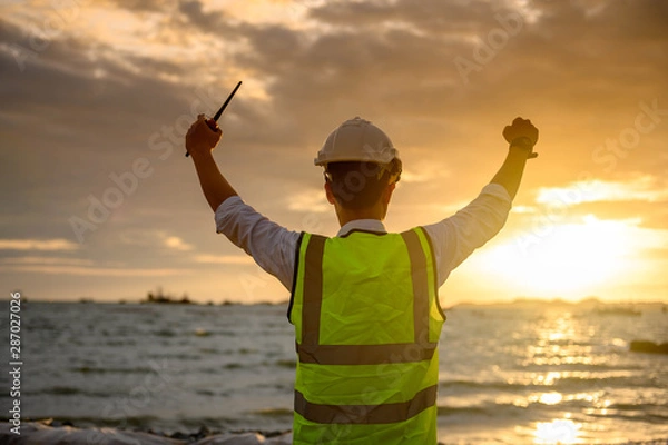Fototapeta Success Engineer standing back during sunrise overlay with sea. The concept of engineering construction