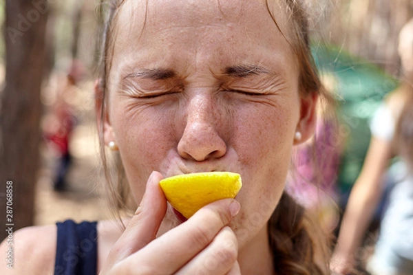 Fototapeta Close up photo of girl eating lemon in the forest