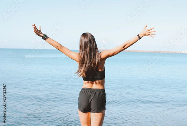 Fototapeta Young slim athletic long hair woman in sportswear doing exercises on the sea beach in morning, healthy lifestyle