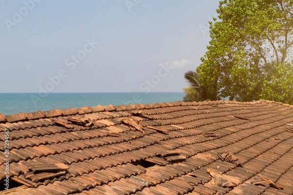 Fototapeta Broken old terracotta tile on a roof on sea background. Toned with sunlight. Summer time.