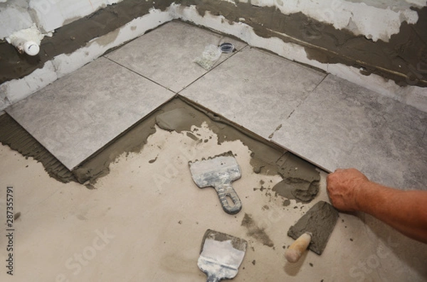 Fototapeta Builder installing ceramic tile on the floor, bathroom flooring. Floor tiling