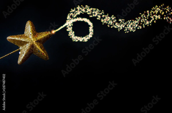 Obraz Christmas golden star magiс wand with fairy blowing dusty glitter curved line, isolated closeup on black background, template for border design with free space for text