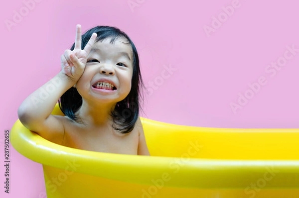 Fototapeta Three year old kid bathed in a yellow basin and playing with camera. Soap bubbles and kid bathing.
