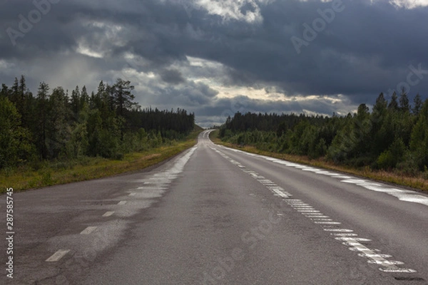 Fototapeta Road across Swedish Lapland is lit with ray of sunlight from under a thundercloud