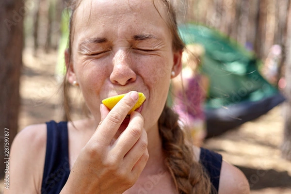 Fototapeta Emotional face of girl eating lemon in the forest