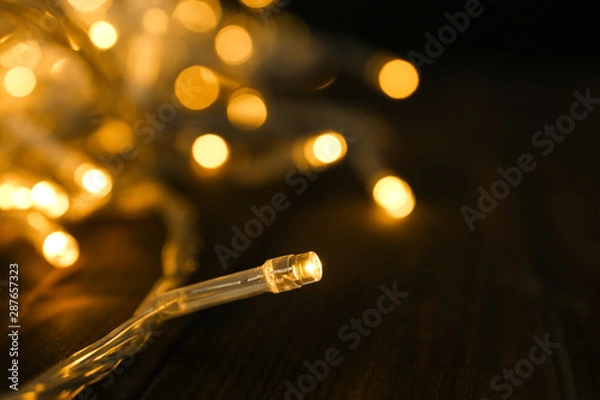 Obraz Glowing Christmas lights on table, closeup view