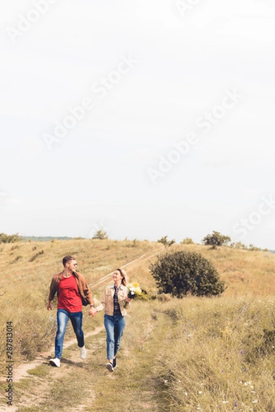 Obraz attractive woman with bouquet and handsome man smiling and holding hands