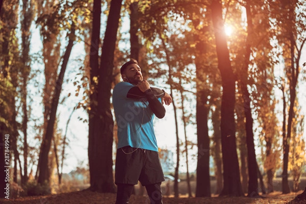Obraz Young man stretching bodies, warming up for jogging in public park.