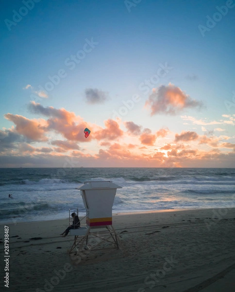 Obraz people sit on lifeguard stand with people playing surfboard in background with sunset in scarborough beach western australia