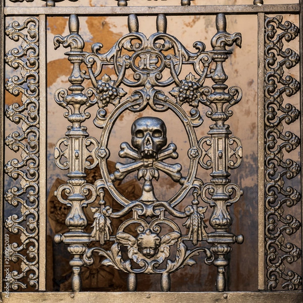 Fototapeta Italy, Apulia, Metropolitan City of Bari, Locorotondo. May 30, 2019. Skull and bones in the ironwork gate to a mausoleum in the local cemetery.