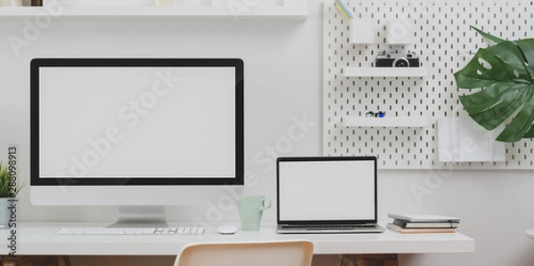 Fototapeta Desktop computer and blank screen laptop with copy space and office supplies in minimal office room