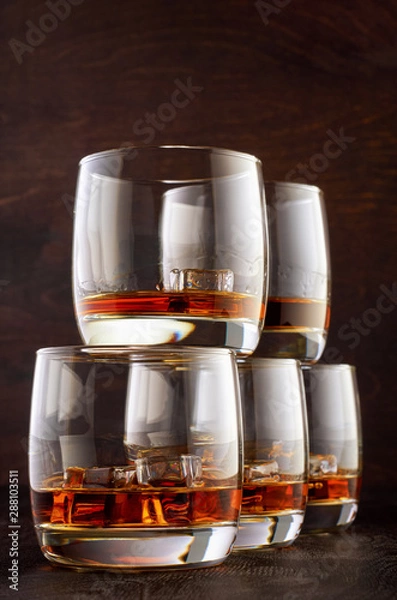 Fototapeta Five glasses of Scotch and ice stand in a pyramid on a wooden table.