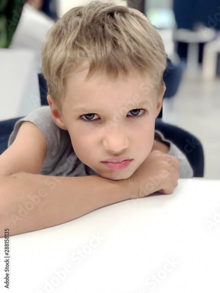 Fototapeta portrait of a blonde boy in restaurant at the table. Unhappy boy's face