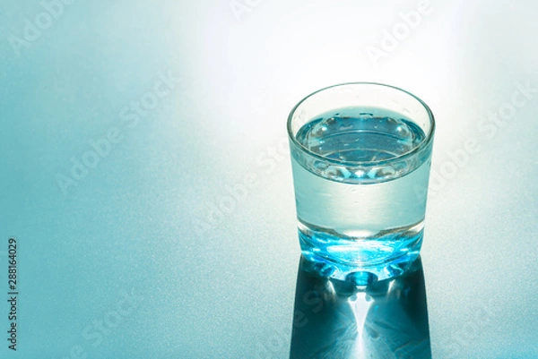 Fototapeta Glass of water with reflecting shadows on blue background.  Healthy food concept. Top view. Copy space